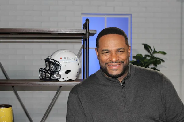 Smiling Jerome Bettis seated next to a white football helmet with an Aire Serv logo.
