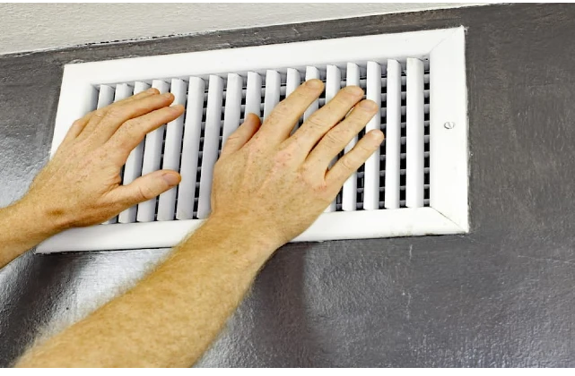 Homeowner testing their heating and cooling system by placing hand near vent