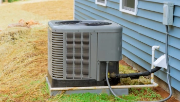 An outdoor AC unit at the side of a house surrounded by mostly dry grass