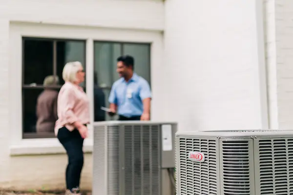 Large outdoor HVAC unit and customer and technician discussing service details in background.
