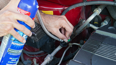 Close-up of person holding blue can of AC Avalanche refrigerant beside machine parts.