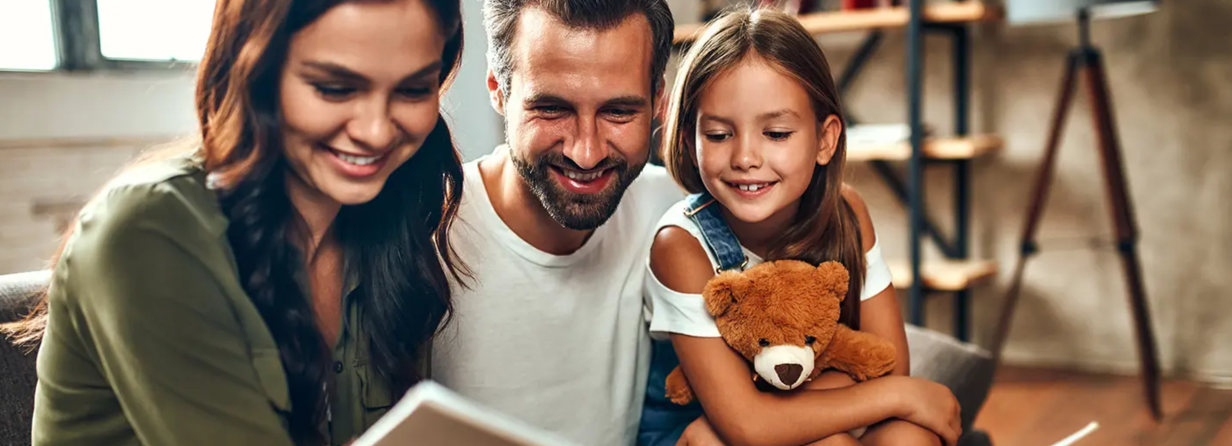 Smiling mother, father and daughter holding teddy bear in residential interior.