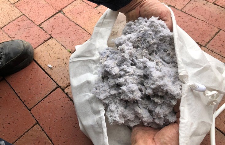 Hands reaching into bag of white dryer vent lint dust.