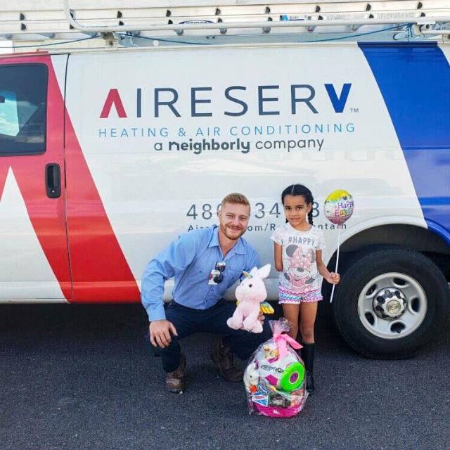 An Aire Serv employee with a stuffed animal next to a child holding a balloon in front of Aire Serv van