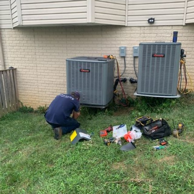 Aire Serv employee working on Amana condenser outside of tan home.