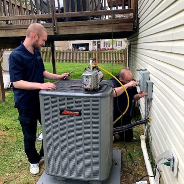 Aire Serv employees working on Amana AC condenser outside of white paneled home.