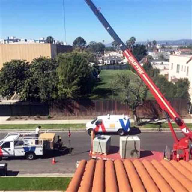 View from the roof of an Aire Serv team on the ground with a new AC system being loaded onto crane