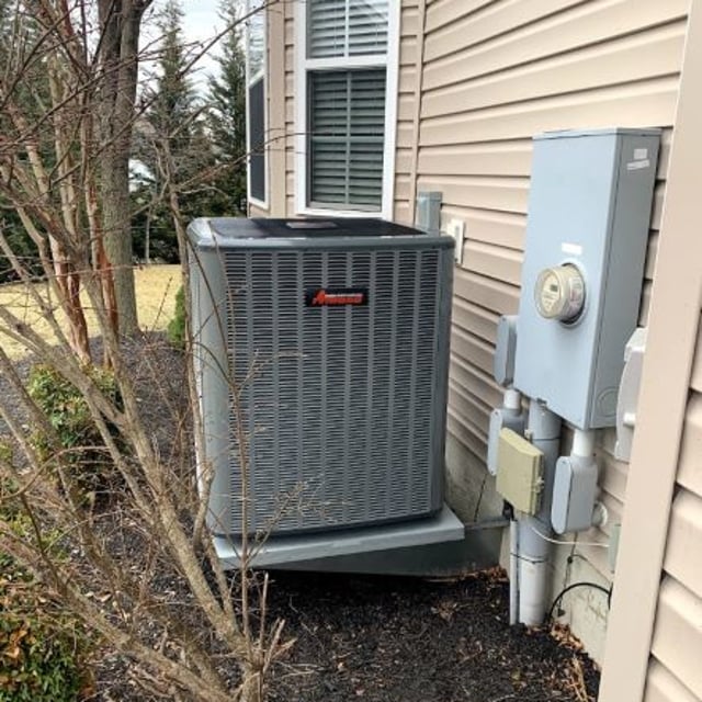 Amana AC condenser mounted on metal platform outside of cream paneled home.