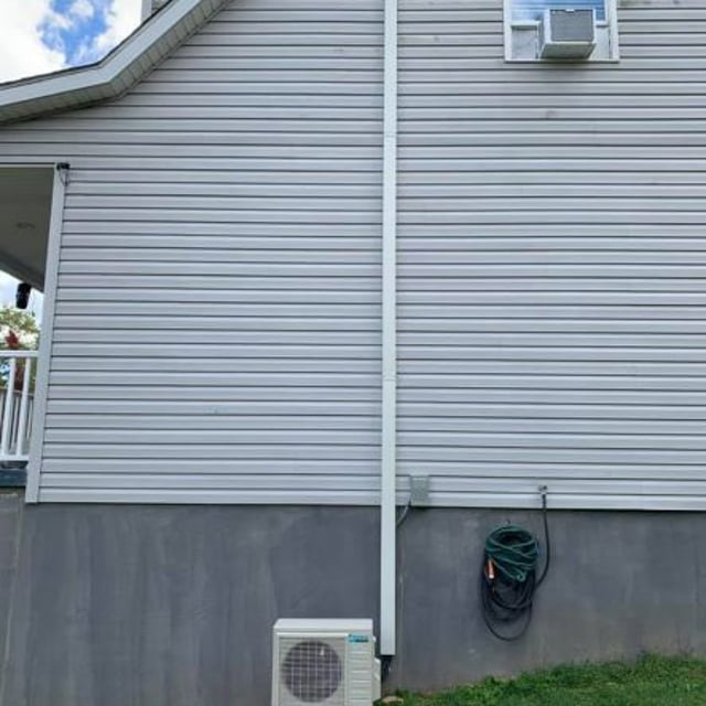 Daikin mini split system condenser outside of white paneled home.