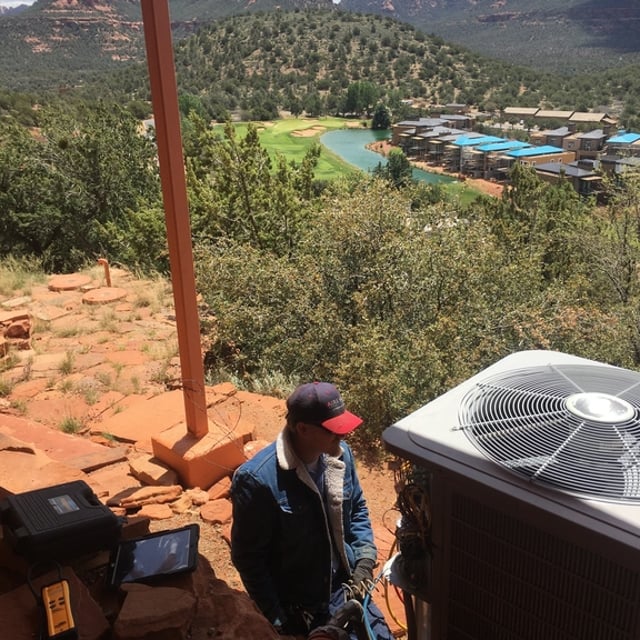 Individual working on an outside unit with beautiful scenery of mesas, trees, mountains, and more