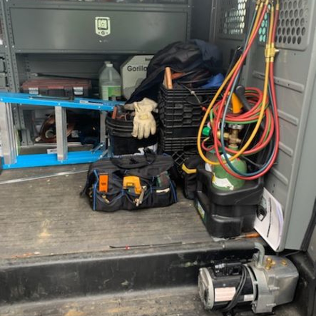 Inside the back of an Aire Serv van with ladder, tool chest, and HVAC unit testing wires.