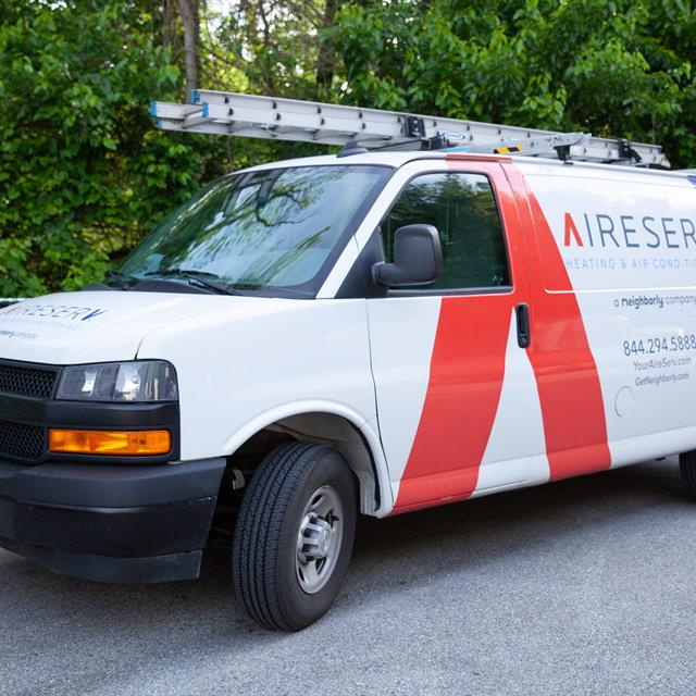 A white Aire Serv work van with branding on the side and a ladder on top