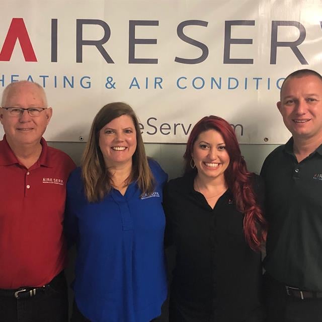 four people in front of aire serv sign