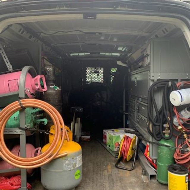 inside the back an Aire Serv van with different refrigerant canisters and tool chest.