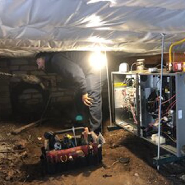 technician drilling a hole underneath a house