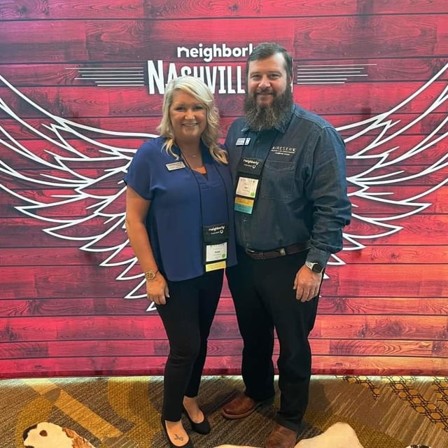 two people standing for photo in front of a backdrop with wings