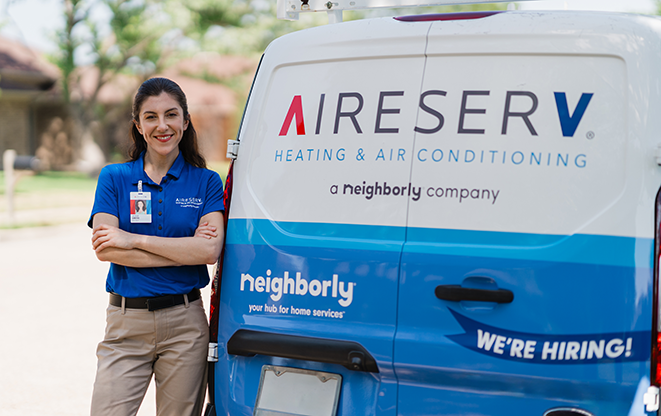 Smiling female Aire Serv professional leaning against branded truck.