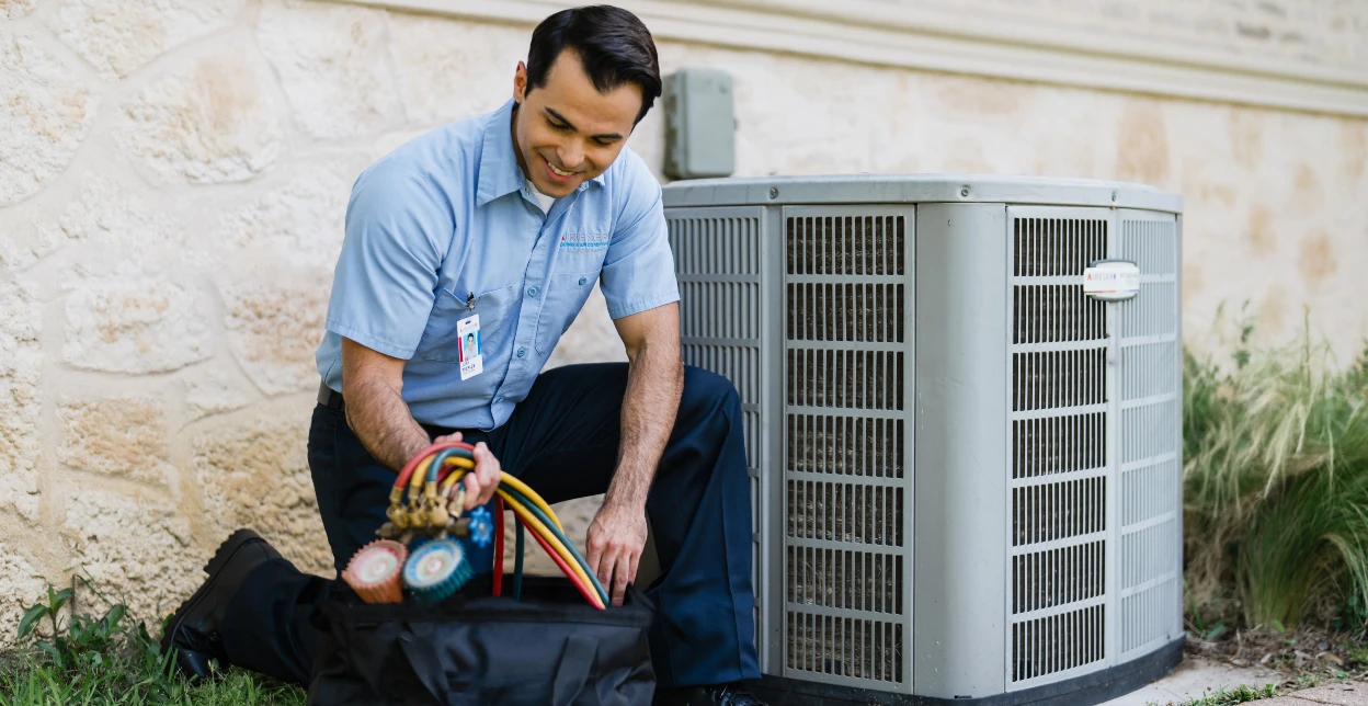 Aire Serv technician kneeling in front of an air conditioning unit taking tools out of their bag.