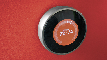 Smart thermostat on dark orange wall reading 72-74