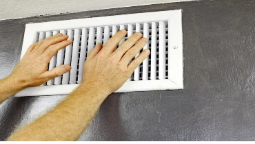 Homeowner testing their heating and cooling system by placing hand near vent