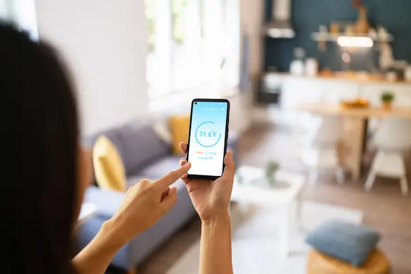 A woman adjusts the temperature in her home using an application on her smartphone.